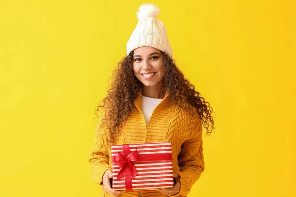 若いですアフリカ系アメリカ人女性で暖かい帽子でクリスマスプレゼント上の黄色の背景 — ストック写真