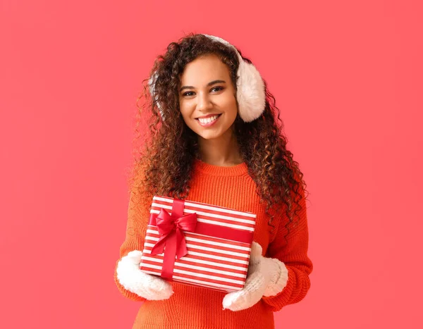 若いですアフリカ系アメリカ人女性で暖かいですEarmuffとともにクリスマスプレゼントオン赤の背景 — ストック写真