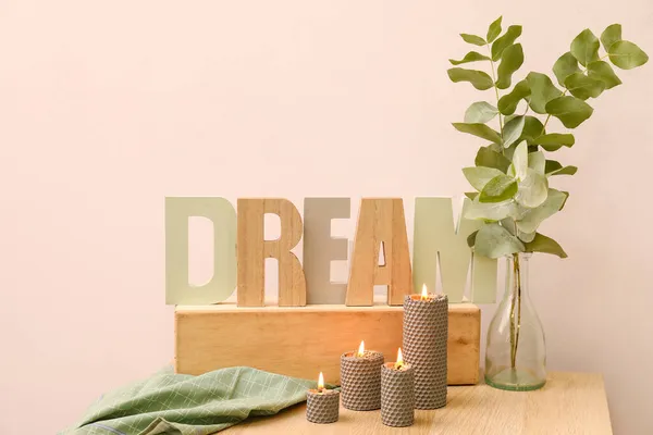 キャンドル ユーカリの枝と言葉で花瓶を燃焼光の壁の近くの木製のテーブルの上に夢 — ストック写真