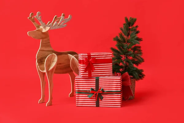 木のトナカイとクリスマスツリーと赤の背景にプレゼント — ストック写真