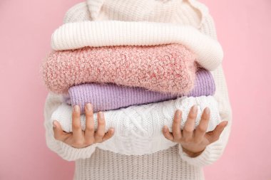 Woman with beautiful manicure holding stack of different sweaters on color background clipart