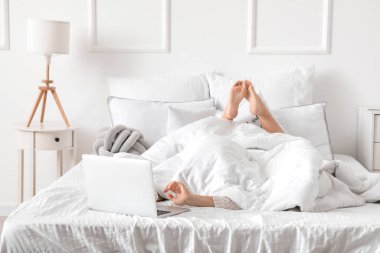 Dizüstü bilgisayarı olan genç bir kadının yatakta yattığı sabah.