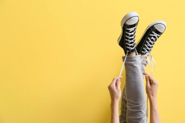 Sarı arka planda beyaz bağcıklı spor ayakkabılı kadın.