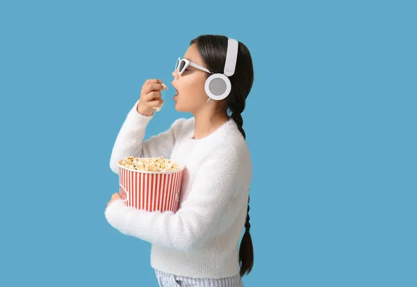 幸せなかわいいです女の子でヘッドフォンとサングラス食べるポップコーン上の青の背景 — ストック写真