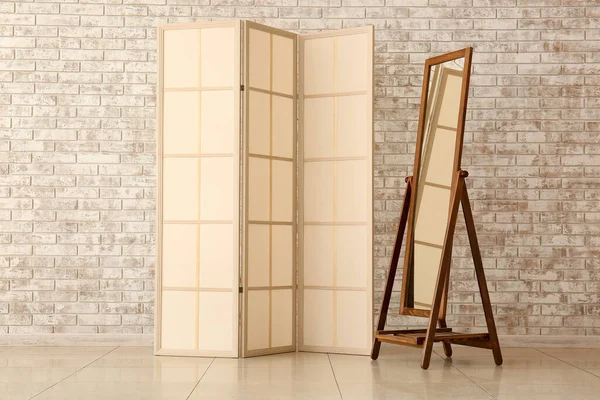 Beige folding screen and mirror near light brick wall