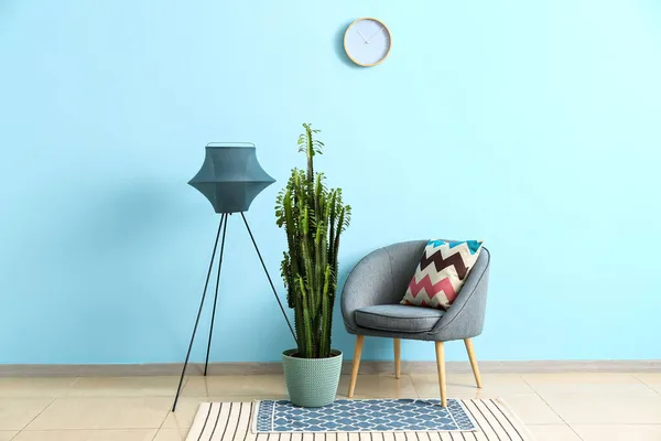 Green cactus with lamp and cozy armchair near blue wall