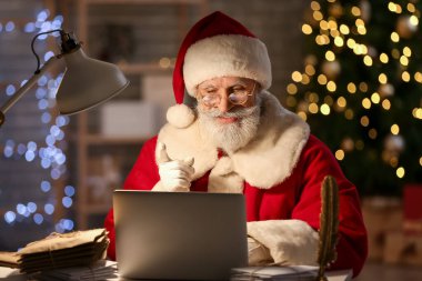 Noel Baba evde dizüstü bilgisayar kullanıyor.