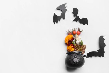 Beyaz arka planda çiçek ve kağıt yarasalarla cadının kazanı.