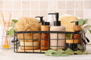 Banyo süngeri, masaj fırçası, kozmetik ürünleri şişeleri ve masa üzerinde okaliptüs dalı olan sepet.