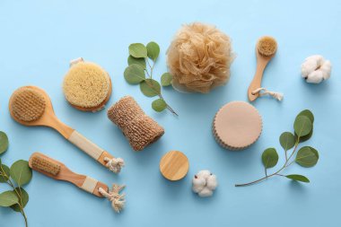 Süngerli, fırçalı ve mavi arka planda bitki dallı banyo malzemeleri.