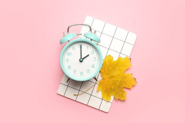 Alarm saati, not defteri ve renk arkaplanındaki sonbahar yaprağı