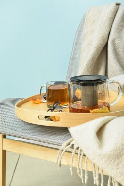 Çay demliği tepsisi, bir bardak sıcak içecek ve sonbahar yaprakları mavi duvarın yanındaki koltukta.