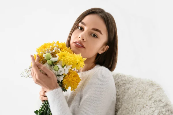 白い背景にアームチェアに座って花の花束を持つ美しい若い女性 — ストック写真
