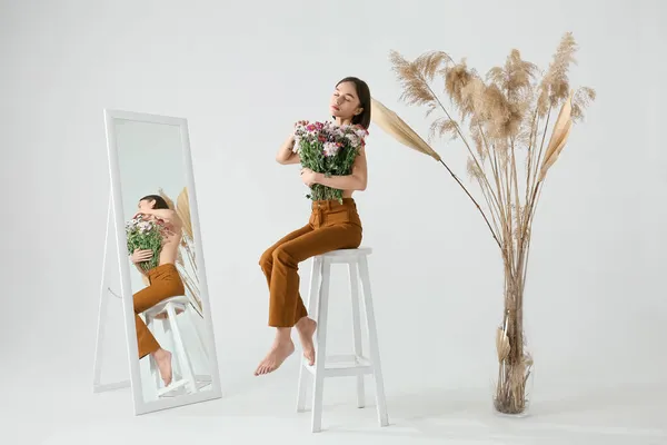 セクシーな若いです女性ともに花の花束上の椅子に座っている光の背景 — ストック写真