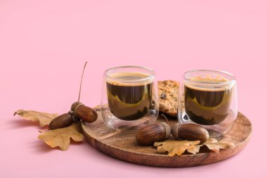 Bir bardak meşe palamudu, sonbahar yaprakları ve pembe arka planda kurabiyeler.