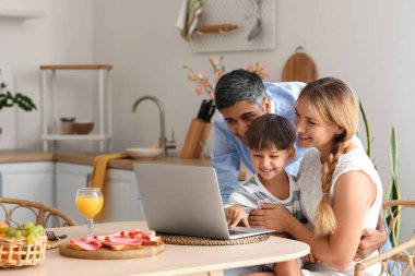 Mutfaktaki masada dizüstü bilgisayar kullanan mutlu bir aile.