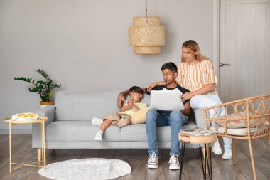 Cep telefonu olan küçük bir çocuk ve ailesi evde dizüstü bilgisayar kullanıyor.