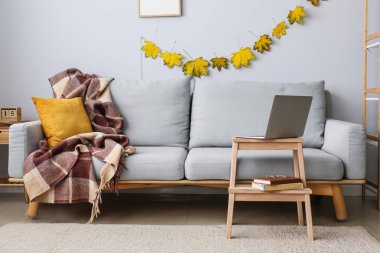 Rahat bir kanepe ve sonbahar yapraklı modern dizüstü bilgisayarlı ahşap masa.