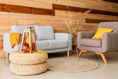 Sonbahar yapraklı mum lambası, rahat kanepe ve ahşap duvarın yanındaki koltuk.