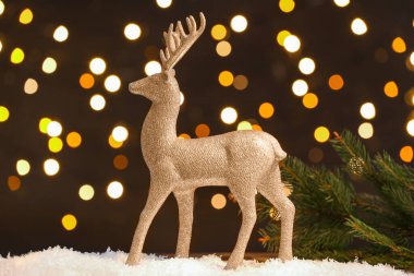 Altın ren geyiği ve köknar ağacı dalı kar masasının üzerinde, koyu arkaplanda.