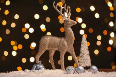 Altın ren geyiği ve Noel dekoru kar masasında, arka planda.