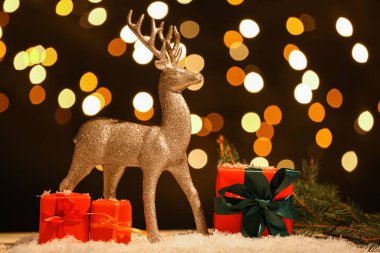 Altın ren geyiği, Noel hediyesi kutuları ve köknar ağacı dalı kar masasının üstünde, arka planda.