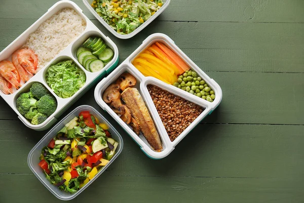 Lunchboxes with tasty healthy food on color wooden background