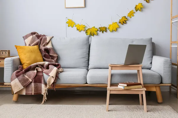 Rahat bir kanepe ve sonbahar yapraklı modern dizüstü bilgisayarlı ahşap masa.