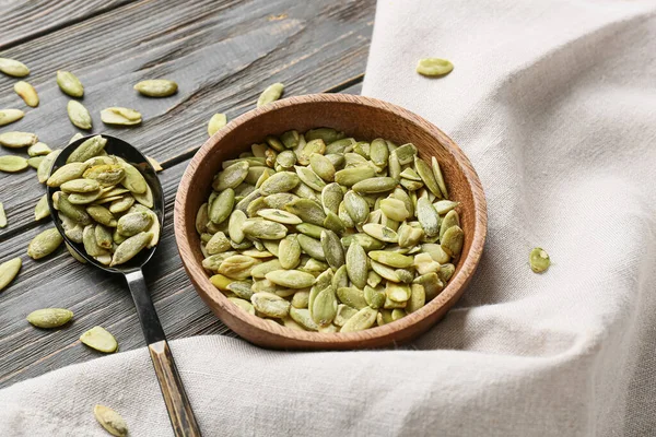 Tahta zemin üzerinde kabak tohumları olan kase ve kaşık.