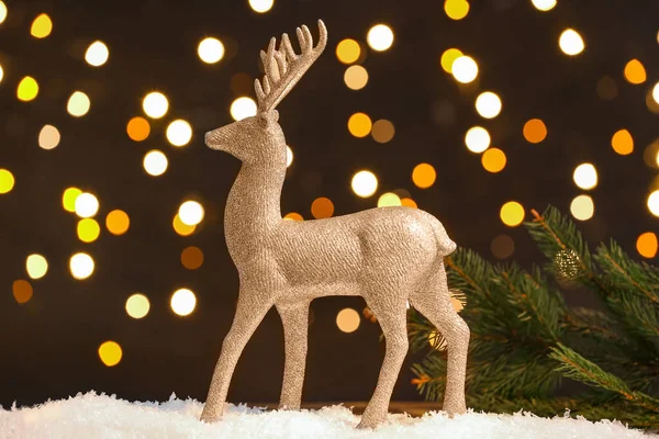 Altın ren geyiği ve köknar ağacı dalı kar masasının üzerinde, koyu arkaplanda.