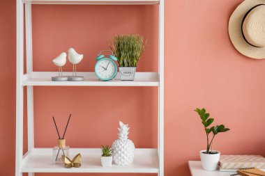 Alarm saati ve pembe duvarın yanında farklı dekorlu bir kitaplık.