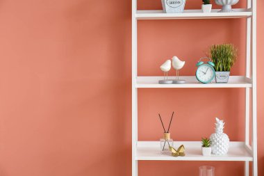 Alarm saati ve pembe duvarın yanında farklı dekorlu bir kitaplık.