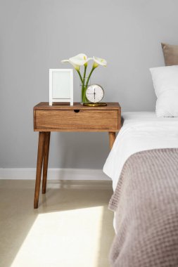 Zambaklı çalar saat ve yatak odasındaki ahşap komodinin üzerindeki çerçeve.