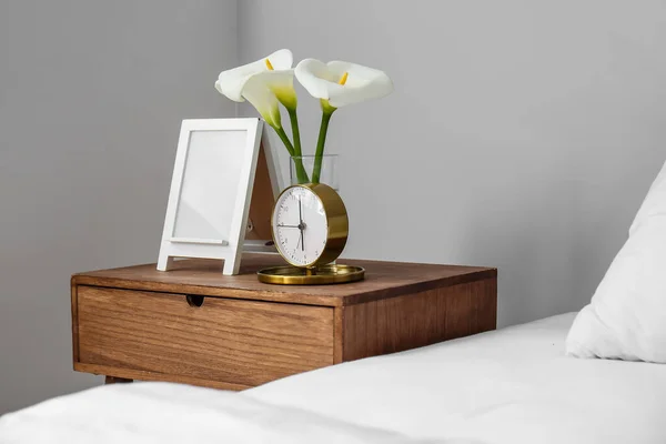 目覚まし時計ともにCalaユリとフレーム上の木製ベッドサイドテーブルでベッドルーム — ストック写真