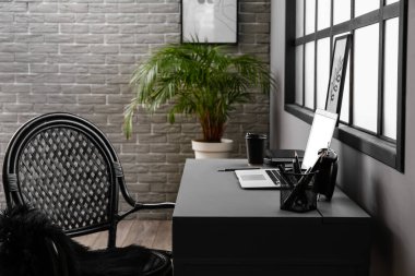 Odanın iç tarafındaki pencerenin yanında dizüstü bilgisayarı olan rahat bir iş yeri