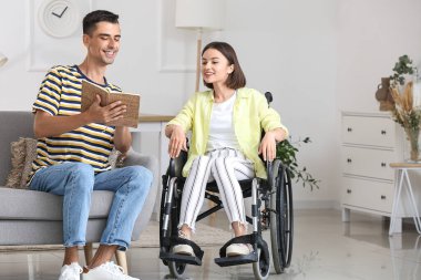 Adam evinde tekerlekli sandalyede karısına kitap okuyor.