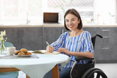 Fiziksel engelli genç bir kadın not defterine evde yazıyor.