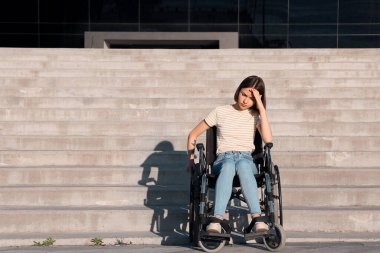 Dışarıda merdivenlerin yanında tekerlekli sandalyedeki depresyondaki genç kadın.