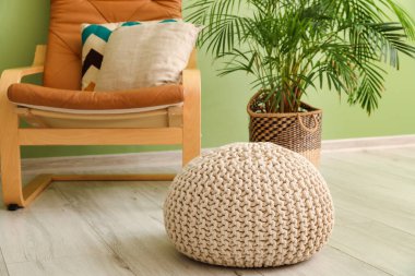 Pouf, koltuk ve çiçek renkli duvarın yanında.