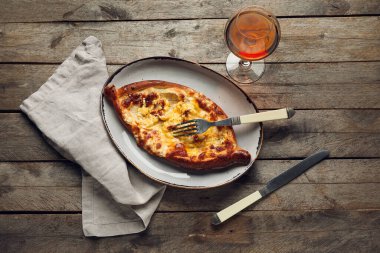 Lezzetli Ajarian Khachapuri tabağı ve ahşap masa arkasında bir bardak şarap.