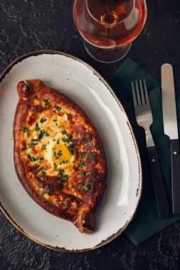 Lezzetli Ajarian Khachapuri tabağı ve koyu masa arkasında bir bardak şarap.