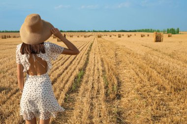 Hasat edilmiş tarla geçmişi olan şapkalı romantik genç bir kadın.
