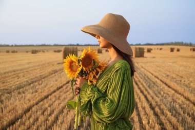 Hasat edilen tarlada ayçiçekleri olan romantik genç bir kadın.