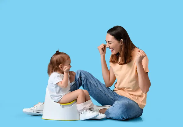 Mother potty training her little daughter on color background