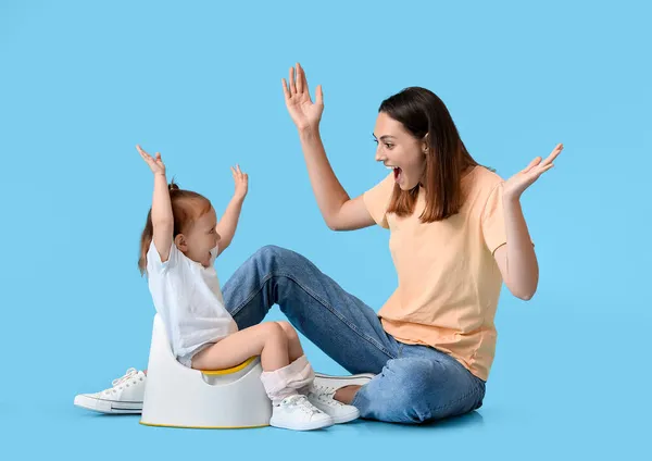 Mother potty training her little daughter on color background