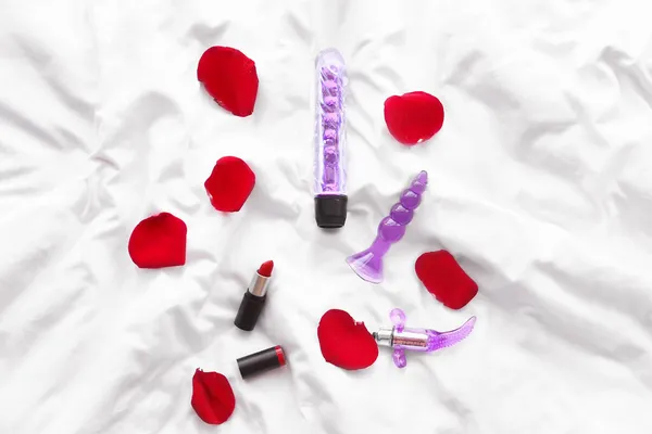 床上不同的性玩具 口红和玫瑰花瓣 — 图库照片