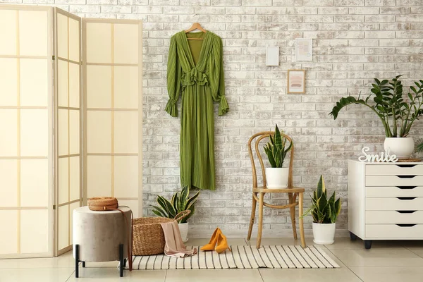 Folding screen, green dress and houseplants near brick wall