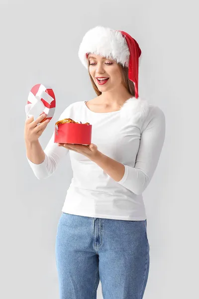 Schöne Junge Frau Mit Weihnachtsmütze Öffnet Weihnachtsgeschenk Auf Grauem Hintergrund — Stockfoto