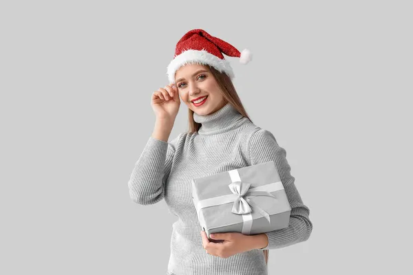戴着圣诞礼帽 头戴灰色背景圣诞礼物的年轻漂亮女子 — 图库照片