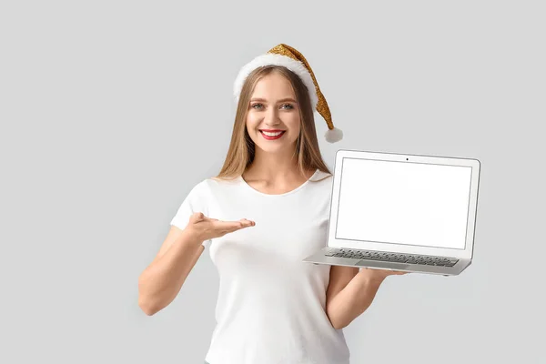 戴着圣诞帽 头戴灰色背景笔记本电脑的年轻貌美的女人 — 图库照片